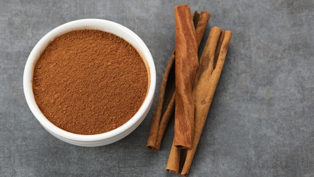 a bowl of cinnamon powder next to cinnamon sticks