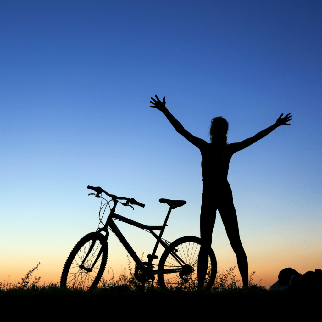 a silhouette of a woman with her arms up next to a bicycle