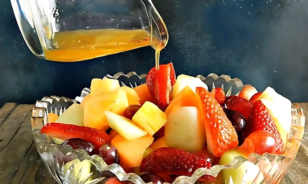 a bowl of fruit salad with a honey being poured into it